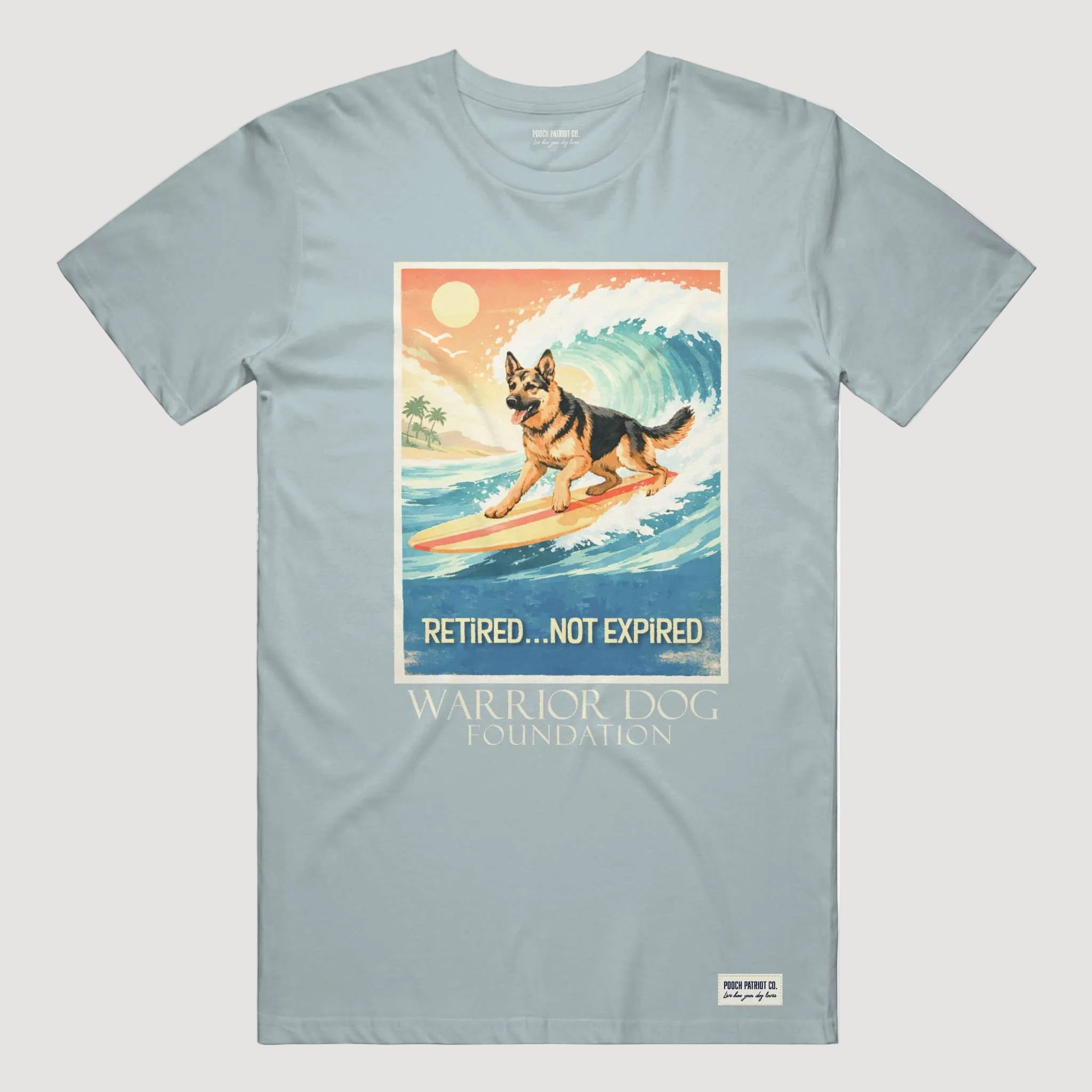 Light blue t-shirt with a graphic of a dog on a surfboard and text 'Retired... Not Expired' by the Warrior Dog Foundation.