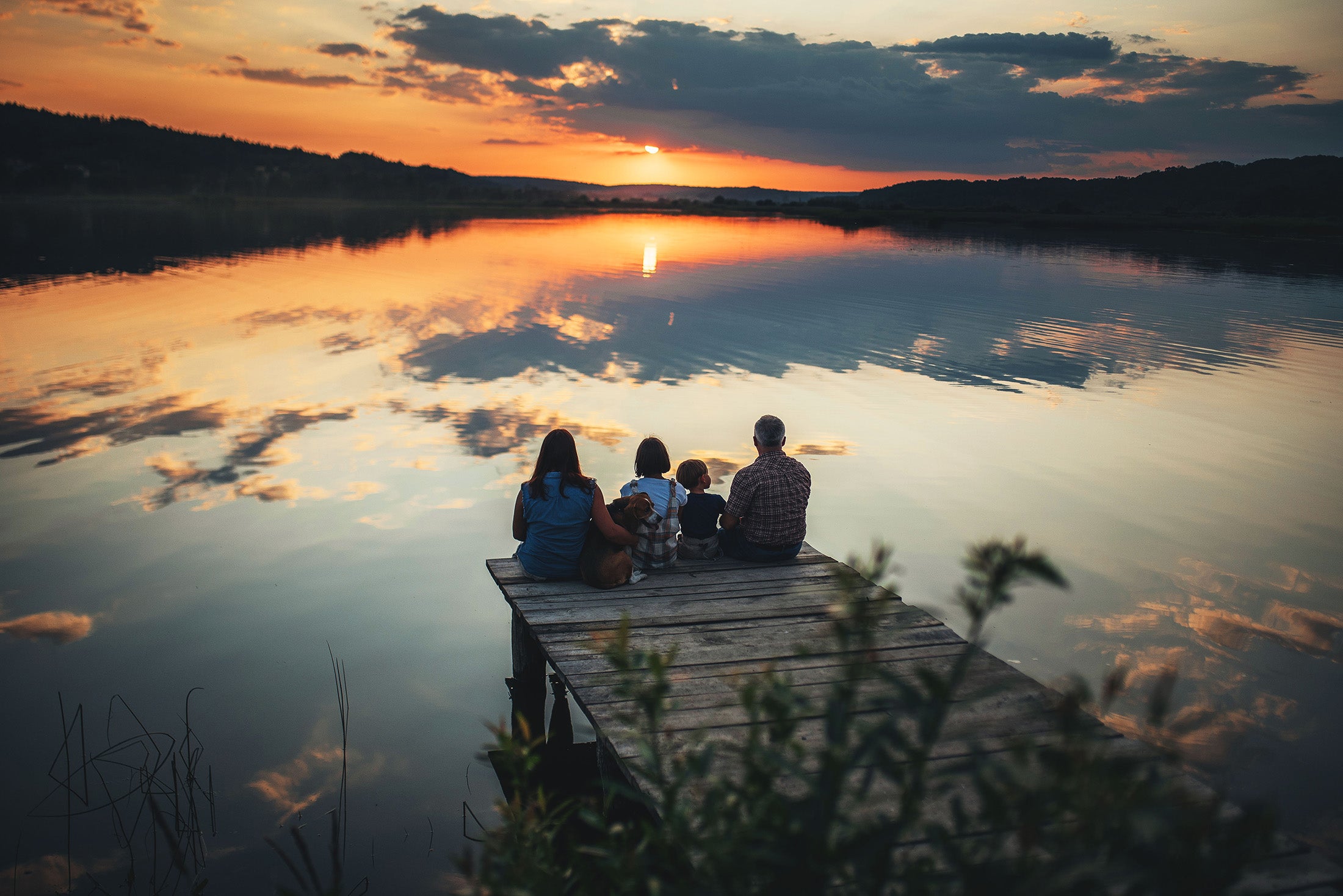 Family sitting on a dock at sunset over a lake